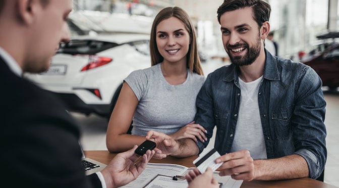 Happy beautiful couple is buying a new car at dealership
