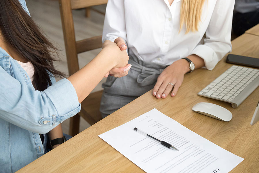 Two women shaking hands over a contract