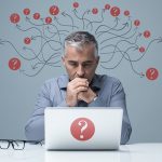 Businessman sat at desk with question marks