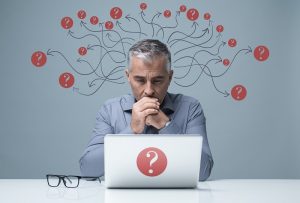 Businessman sat at desk with question marks