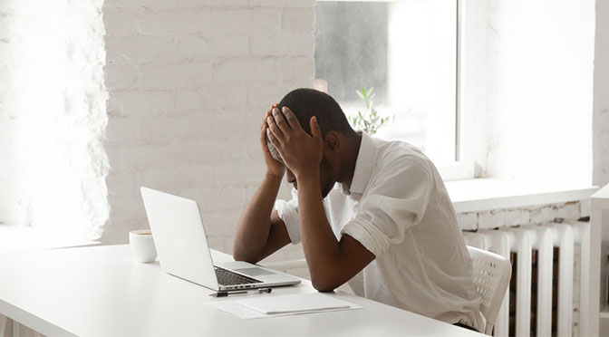 Stressed black businessman in panic after business failure sitting at office work desk in front of laptop