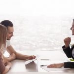 Side view of realtor and young couple sitting at office desk discussing property for sale.