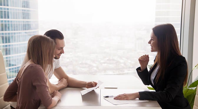 Side view of realtor and young couple sitting at office desk discussing property for sale.